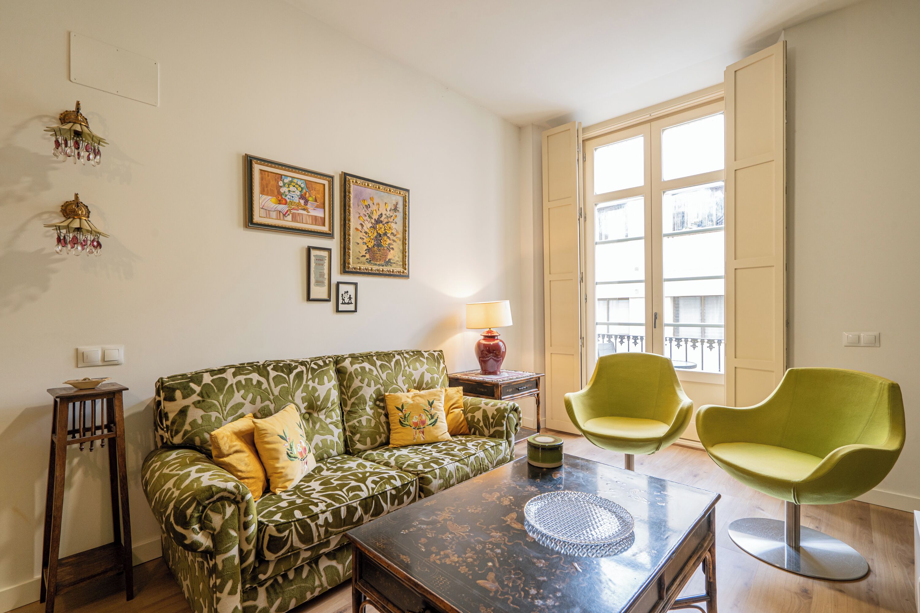 Un salon avec un canapé à motifs verts, deux fauteuils verts, une table basse et une fenêtre donnant sur un paysage agréable.