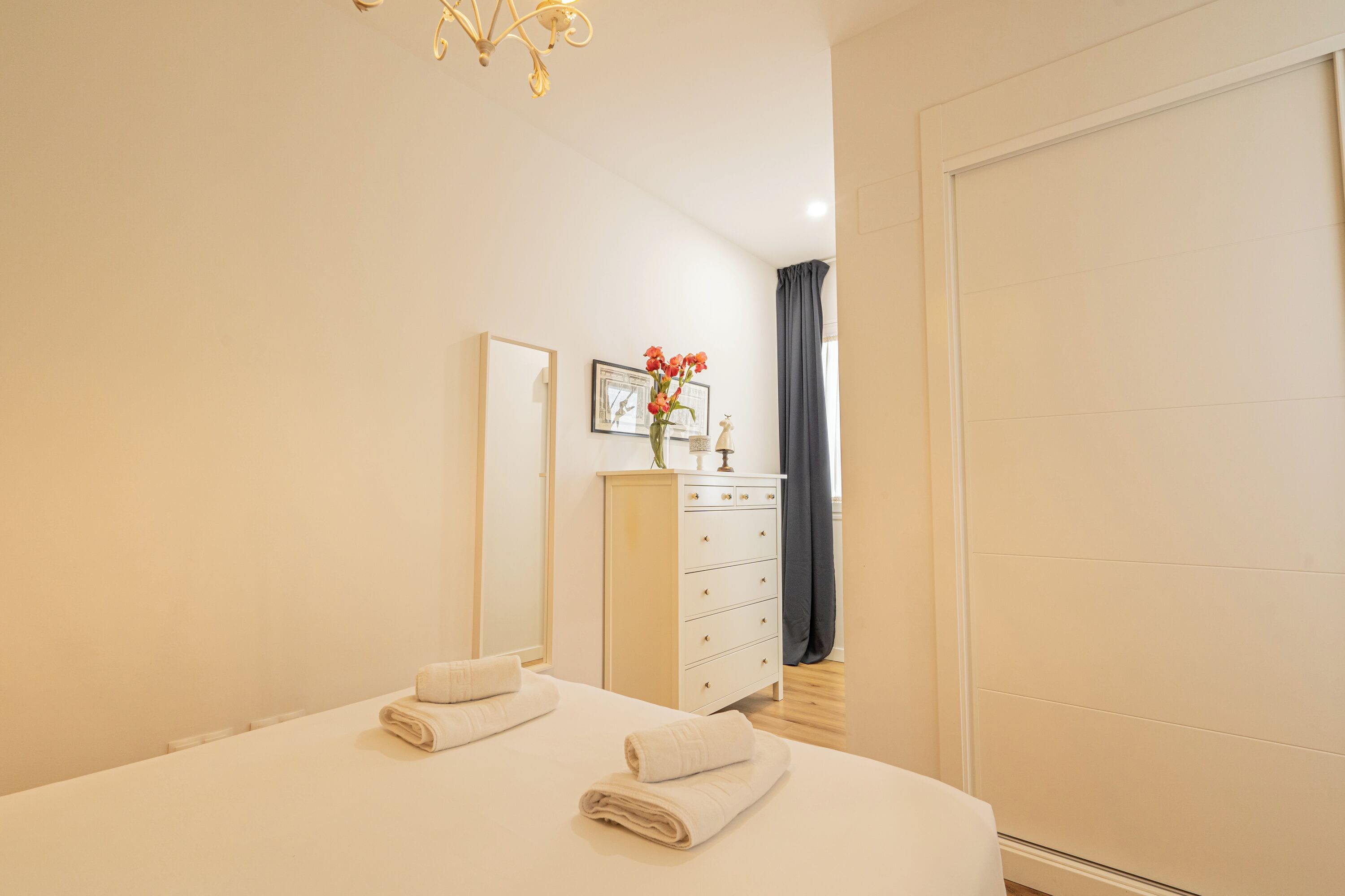 Une chambre d’hôtel avec un lit, une commode, un miroir et une fenêtre avec des rideaux.