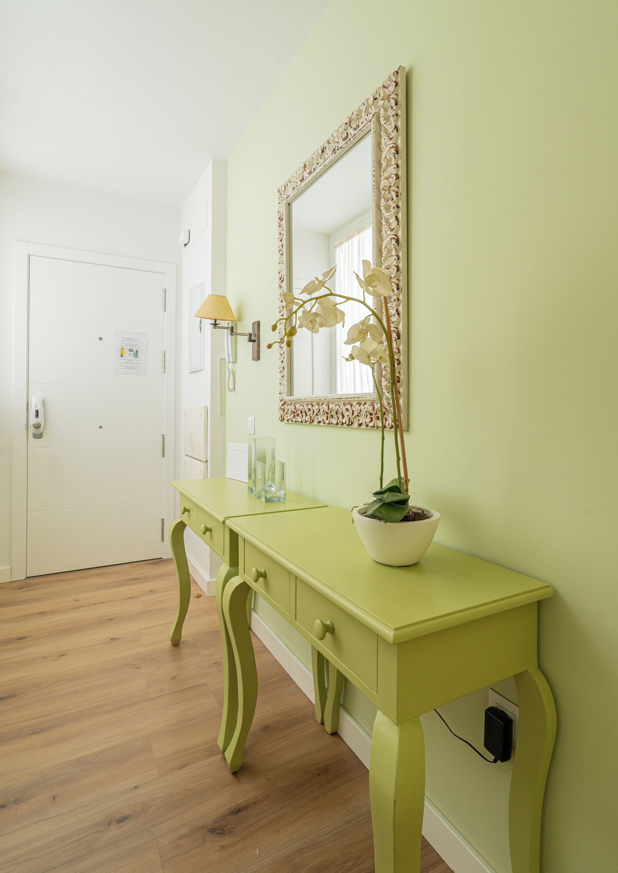 A room with a green vanity, a mirror, a potted orchid, and a white door.