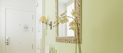 A room with a green vanity, a mirror, a potted orchid, and a white door.