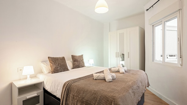 A bedroom with a bed, nightstand, lamp, wardrobe, and a window.