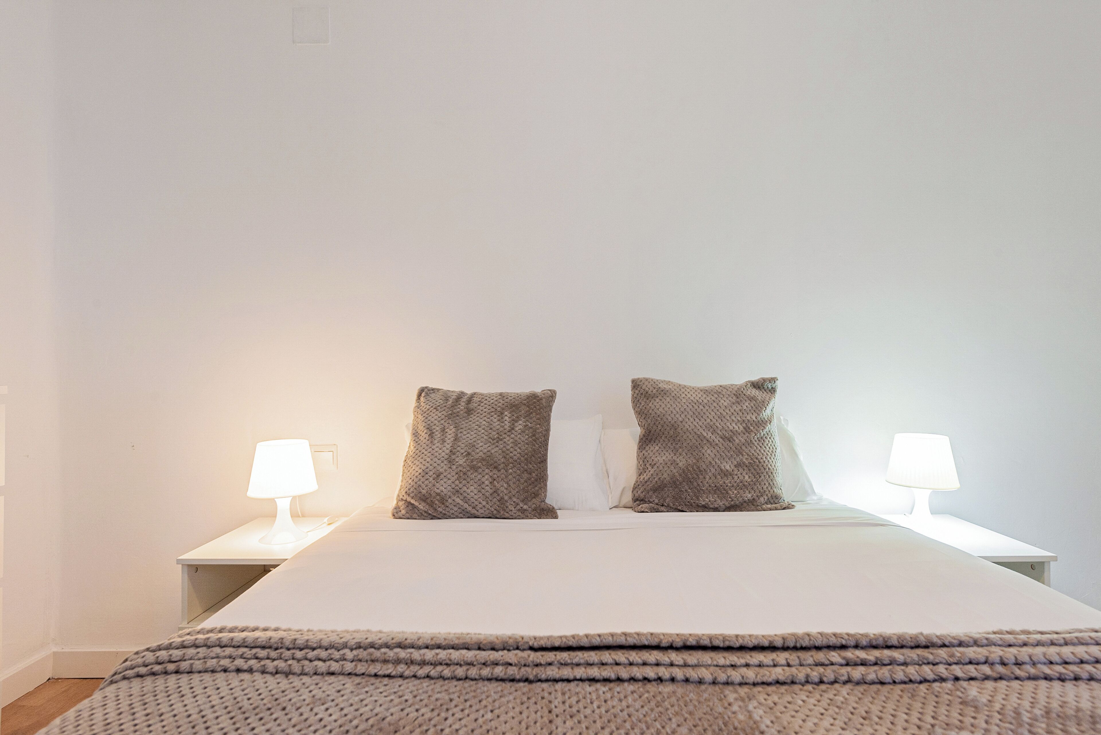 Een opgemaakt bed met twee kussens en twee bedlampjes op witte nachtkastjes.