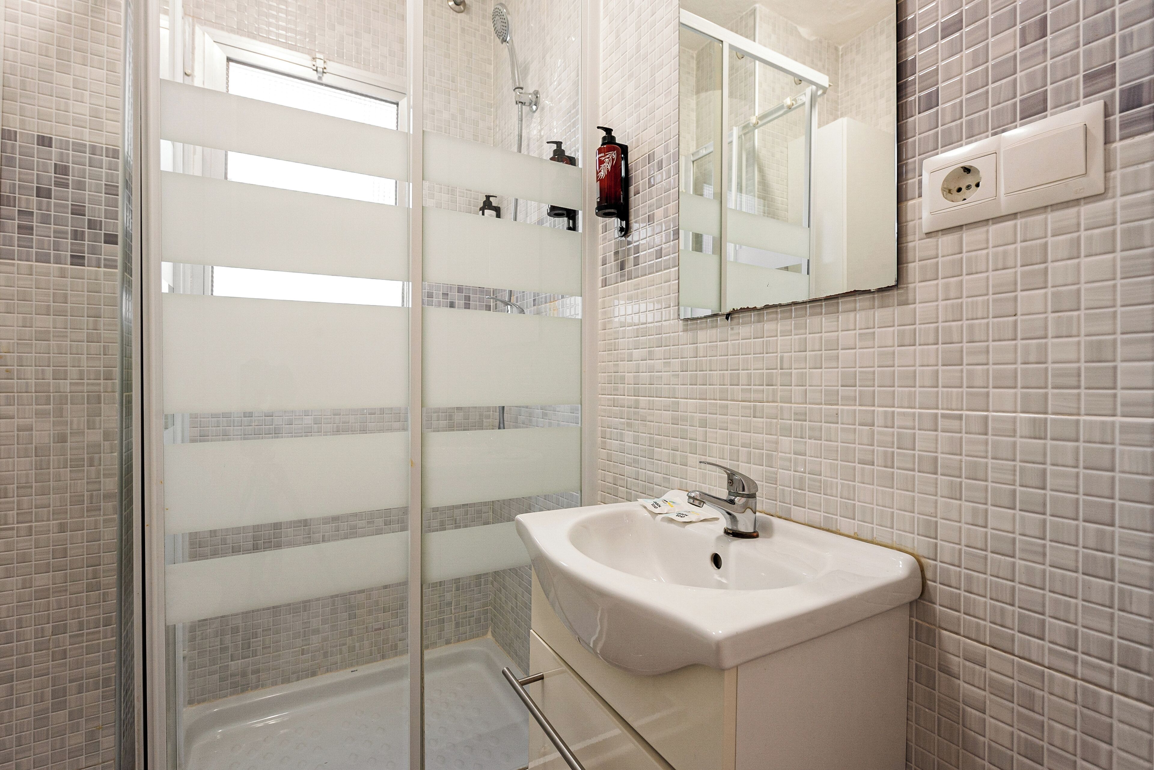 Un bagno moderno con box doccia in vetro, lavandino bianco e specchio sopra.