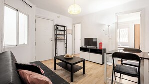 A modern living room with a black sofa, a small black table, and a TV in a kitchen area.