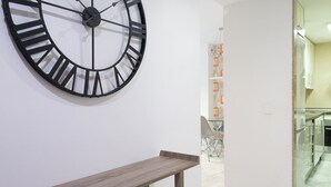 Ein modernes Interieur mit einer großen Wanduhr, einem Holzkonsolentisch und einem durch eine offene Tür einsehbaren Küchenbereich.