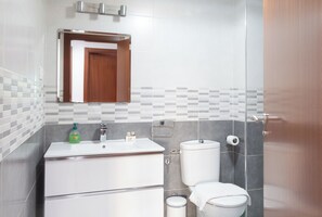 Un baño moderno con lavamanos, espejo e inodoro blancos.