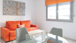 Ein modernes Wohnzimmer mit einer Couch, einem Couchtisch und Sesseln. An der Wand hängt ein Gemälde und es gibt ein Fenster mit Jalousien.