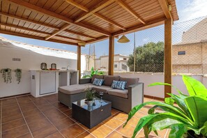 A covered patio area with a sofa, a small table, and a kitchen unit. - Stay U-nique Apartment Ollerias (Málaga)
