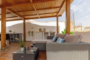 A covered outdoor seating area with a wicker sofa, a table with wine glasses, and a kitchen area in the background. - Stay U-nique Apartment Ollerias (Málaga)