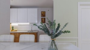 Una cocina moderna con armarios blancos, encimera de mármol y zona de comedor con mesa y sillas blancas.