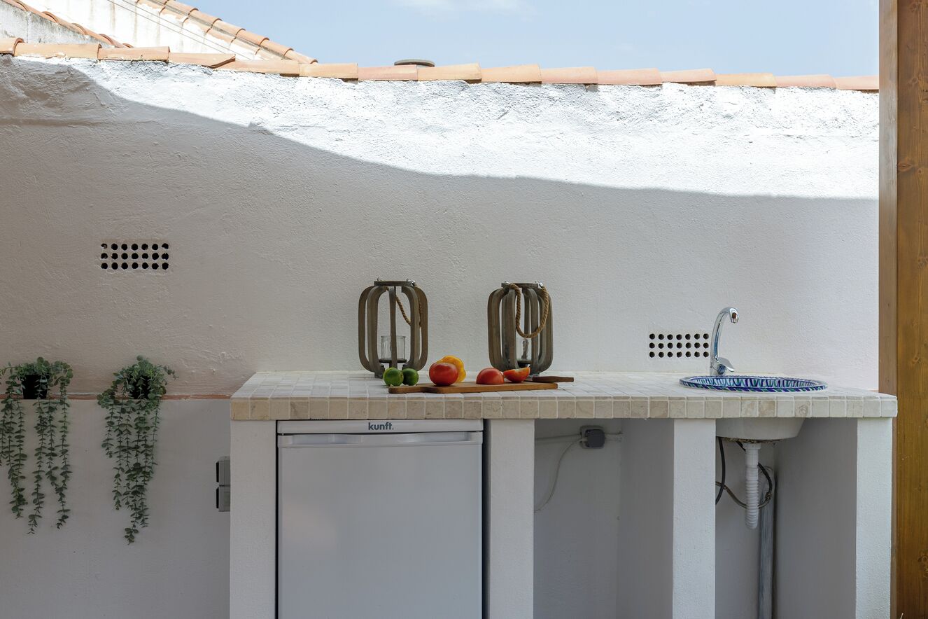 A compact kitchen with a white countertop, a built-in sink, and a small refrigerator.