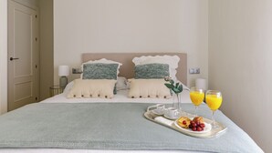 Una cama bien hecha con una bandeja de desayuno, que incluye croissants y fruta, junto con dos vasos de zumo de naranja.