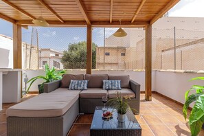 A covered outdoor seating area with a sofa and a table, surrounded by plants and a wooden pergola. - Stay U-nique Apartment Ollerias (Málaga)