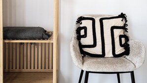 A chair with a geometric patterned cushion, a wooden shelf with a dark cushion, and a plain white wall. - Stay U-nique Apartments Plaza Constitución (Málaga)