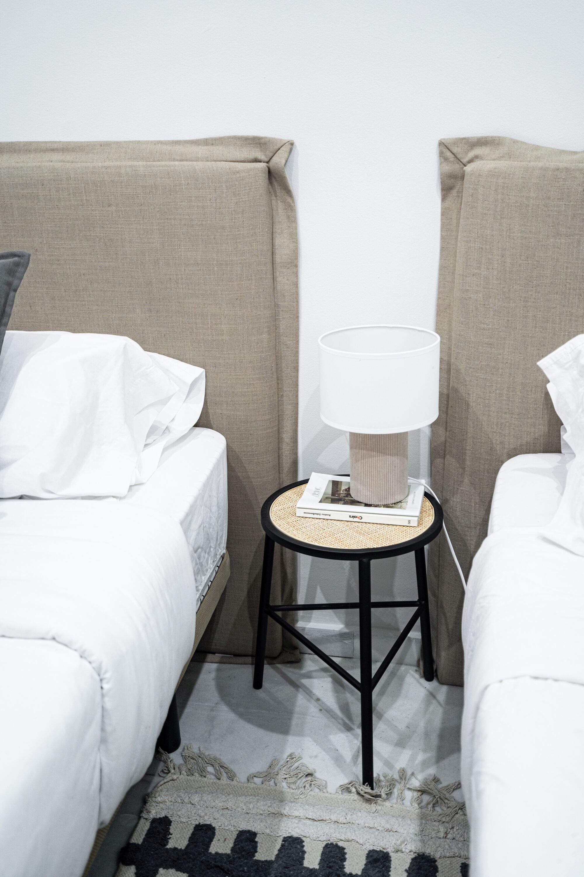 Une chambre d’hôtel avec deux lits simples, une petite table ronde avec une lampe et un tapis tissé.