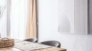 A dining area with a wooden table, grey upholstered chairs, a woven basket, and a textured rug. - Stay U-nique Apartments Plaza Constitución (Málaga)