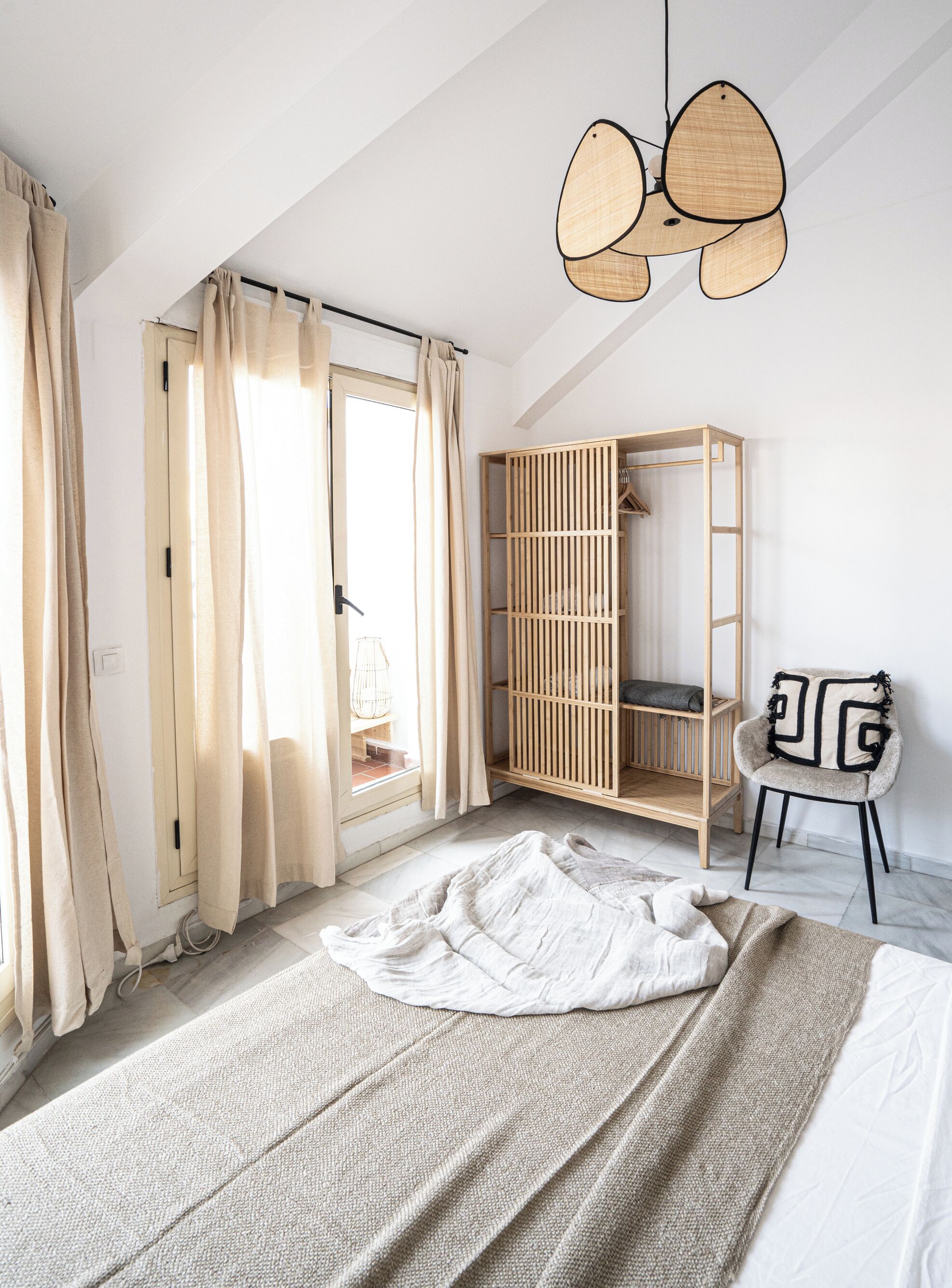 A bedroom with a bed, a wooden wardrobe, a chair, and a hanging light fixture.