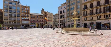 A spacious public square with a central fountain, surrounded by historic buildings with balconies and shops.