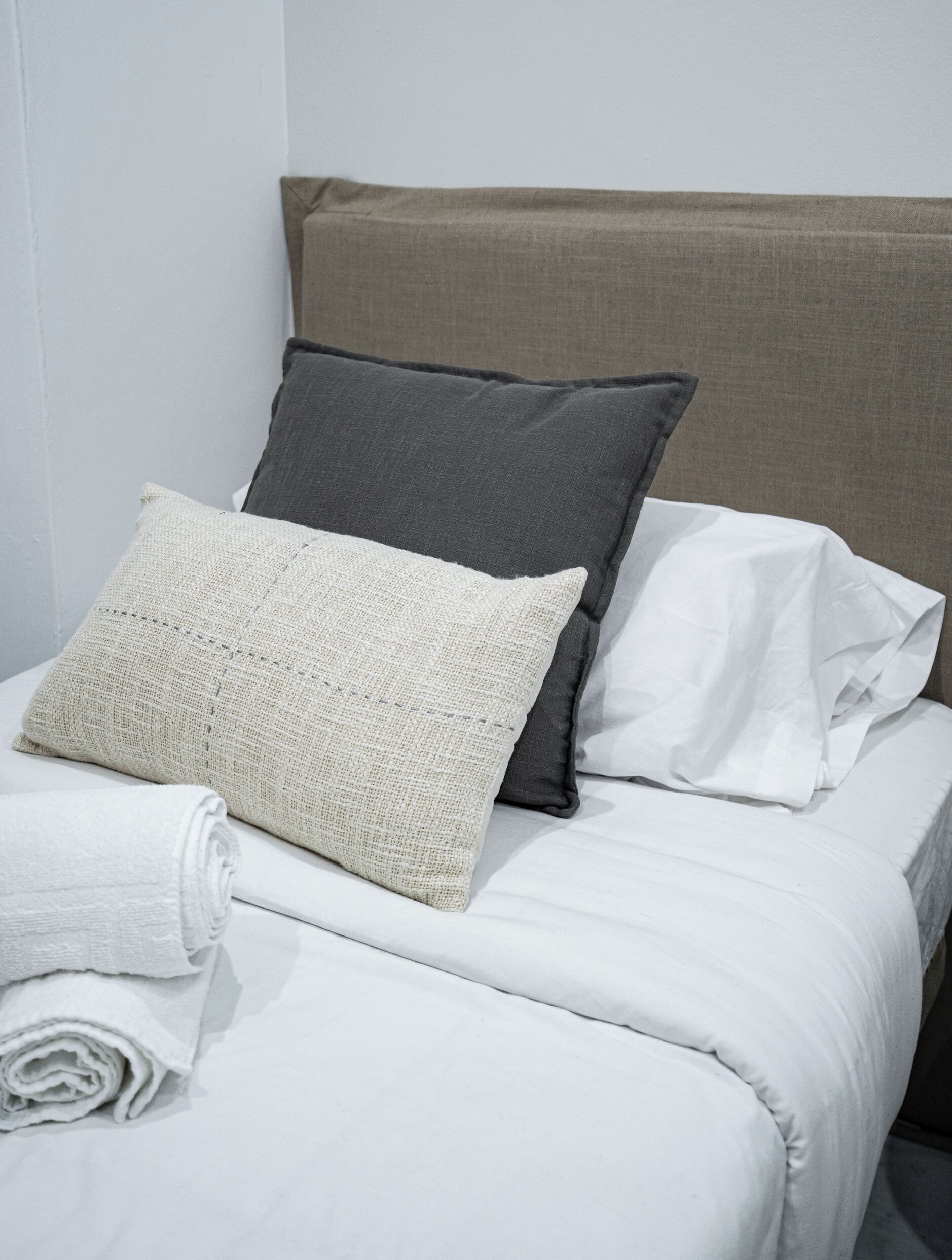 A neatly made bed with white linens and three pillows in different shades.
