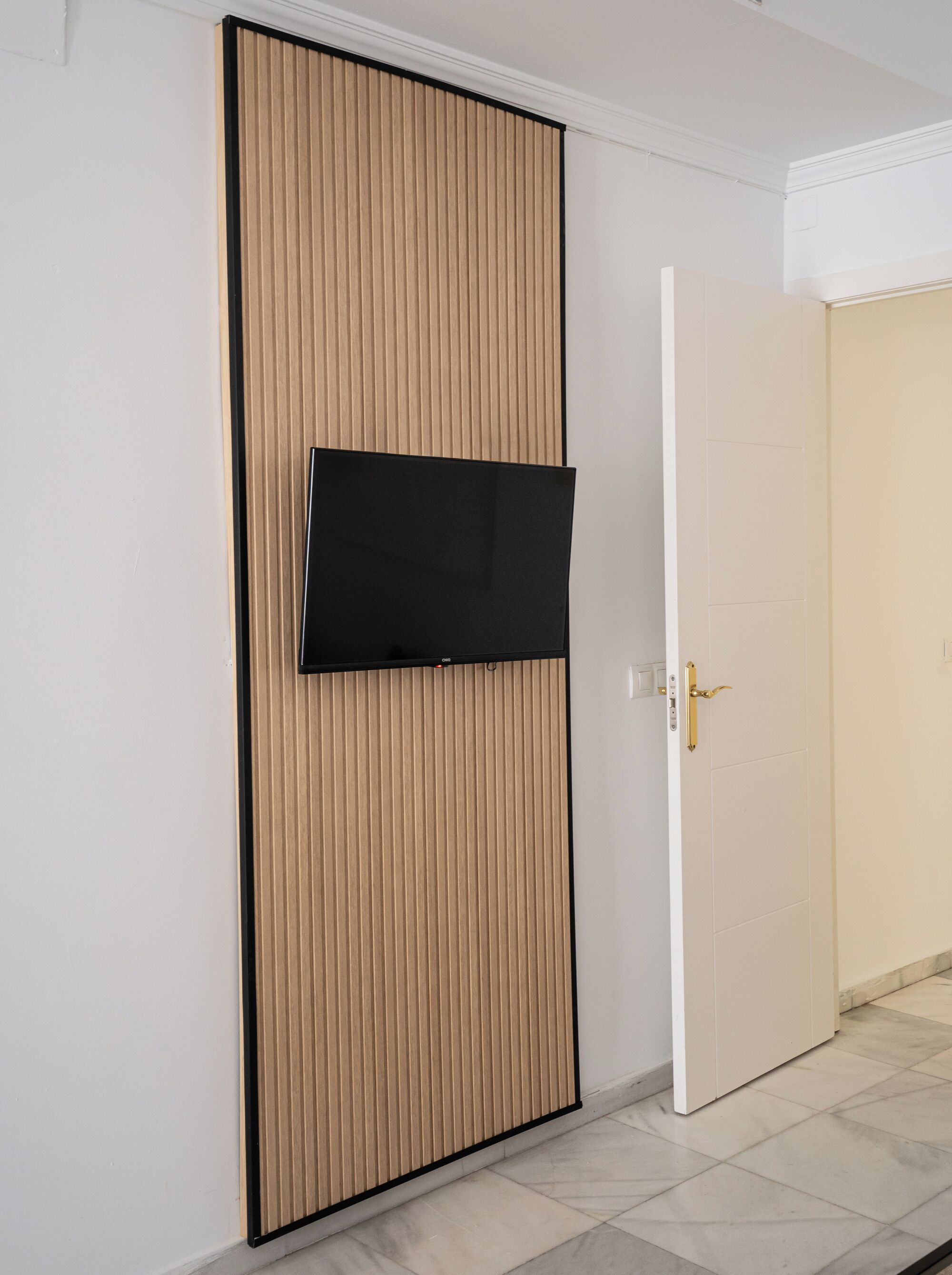 A room with a sliding door, a mounted flat-screen TV, and a white door with a gold handle.