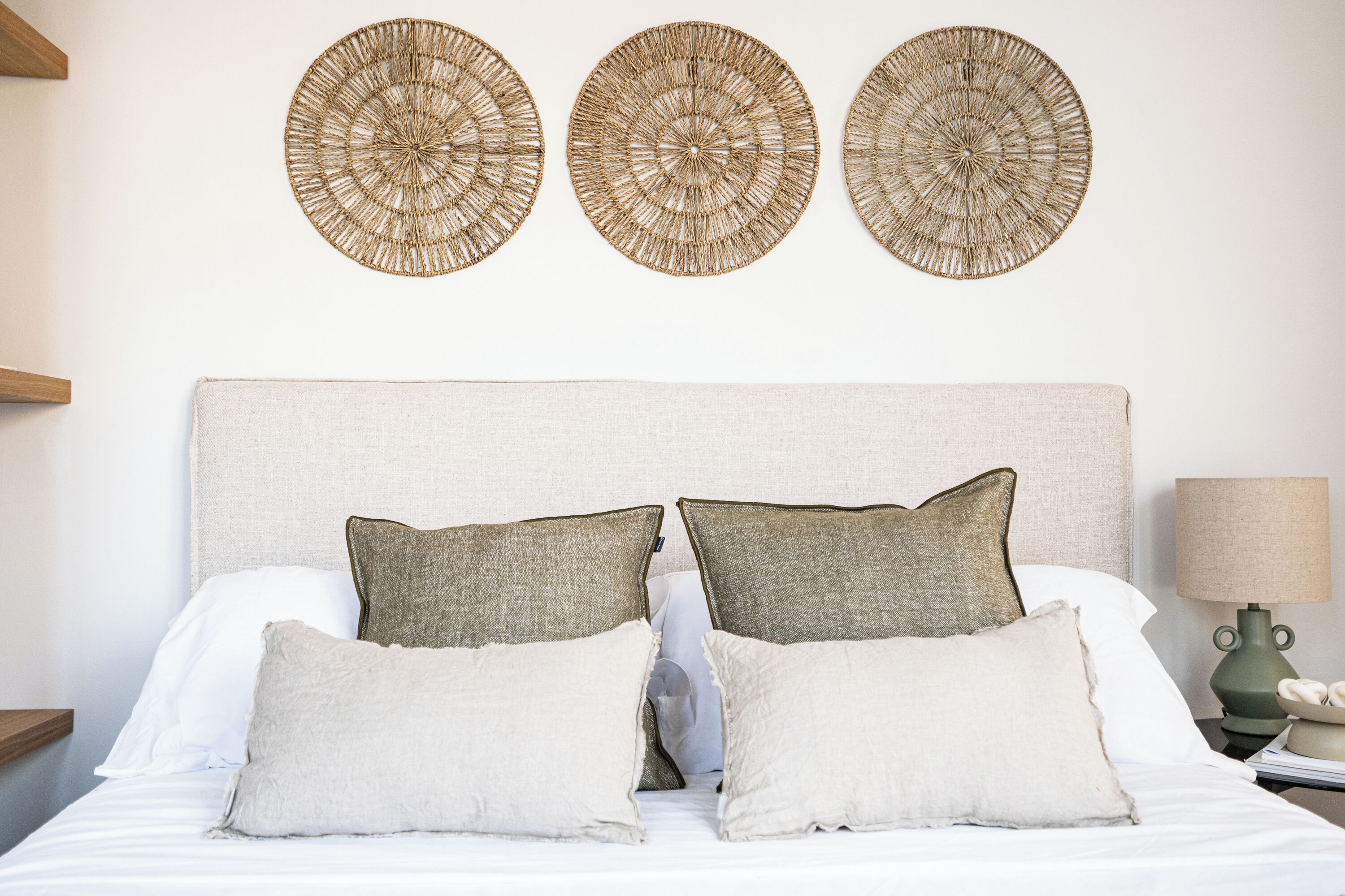 A neatly made bed with three circular wall decorations, a lamp, and a nightstand with a book and a phone.