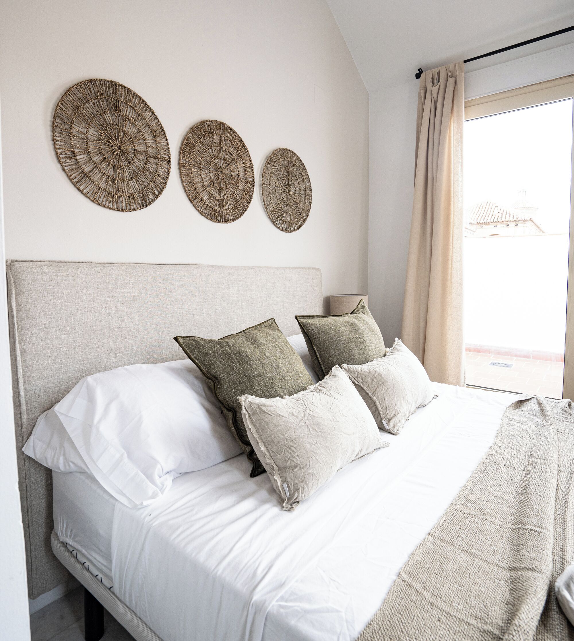 A bedroom with a bed, three wall-mounted circular woven decorations, and a window with curtains.
