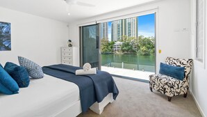 A bedroom with a bed, a chair, a dresser, and a view of a body of water and buildings.