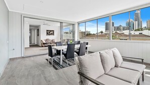 A modern apartment with a dining area, a sofa, and a large window offering a city view.