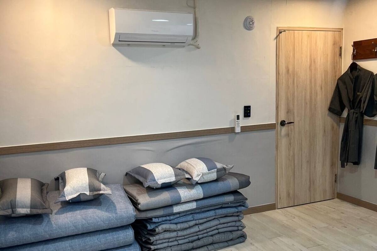 Ein Zimmer mit Holzboden, einem Stapel gefalteter Decken, einer Holztür und einer Klimaanlage an der Wand.
