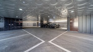 Eine Parkgarage mit moderner Deckenarchitektur, markierten Parkplätzen und einem Auto in der Nähe des Eingangs.