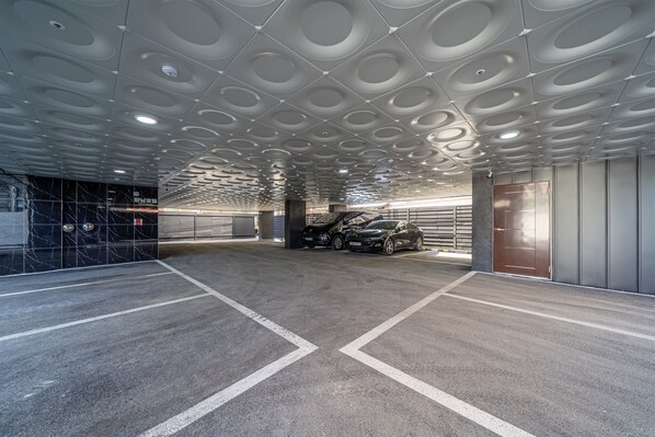 Un parking avec un plafond au design moderne, des emplacements de stationnement clairement délimités et une voiture garée près de l’entrée.