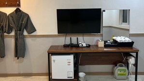 Ein Hotelzimmer mit Holztisch, Flachbildfernseher, Minikühlschrank und kleinem Heizgerät.