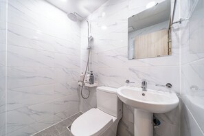 Une salle de bain moderne avec des carreaux de marbre blanc, des toilettes blanches, un lavabo et une douche.