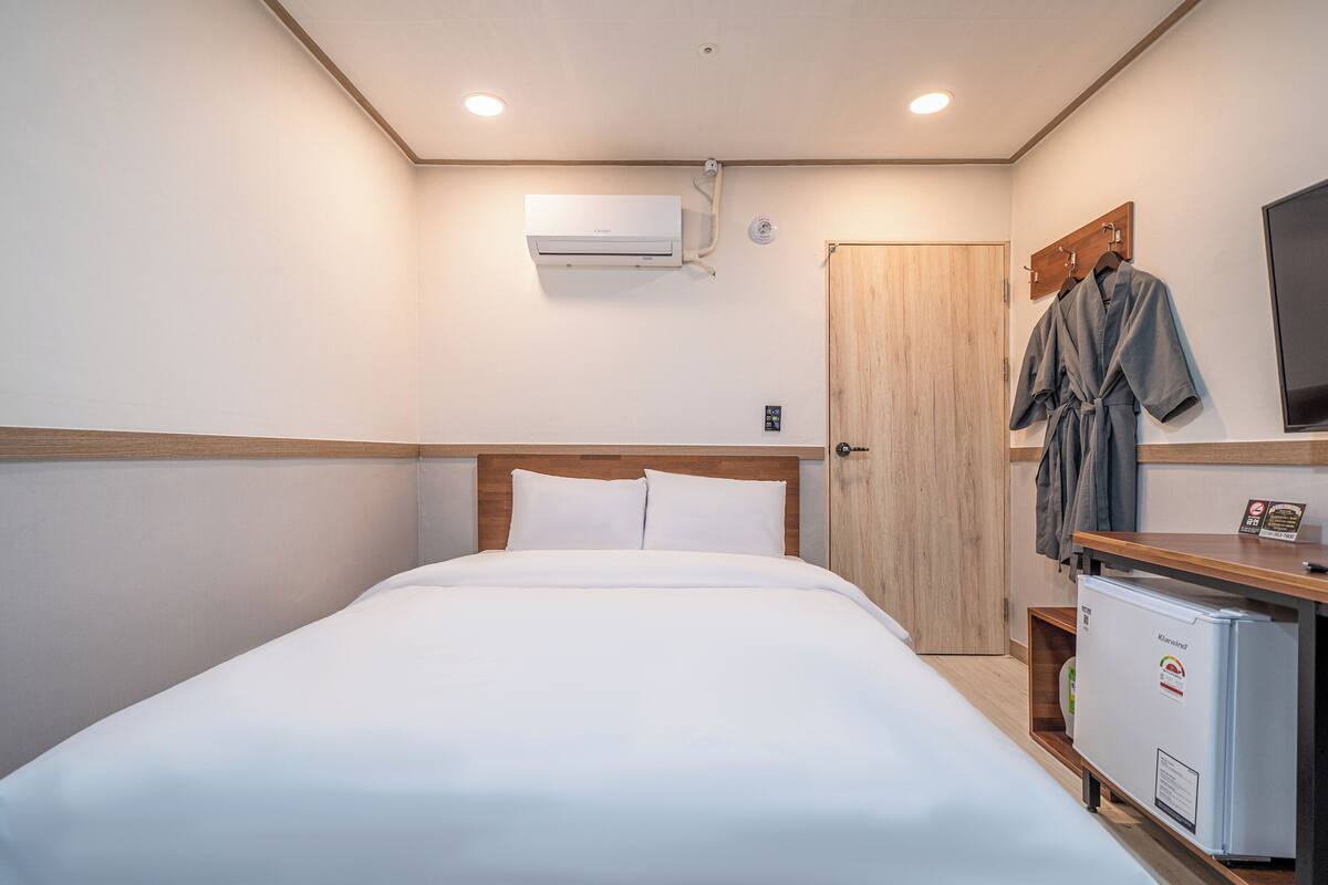 Ein Hotelzimmer mit einem Bett, einem Holzkopfstück, einer Minibar, einer Holztür und einer Wand-Klimaanlage.