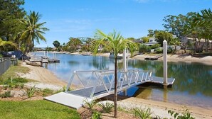 Un área de piscina tranquila con un puente, rodeada de palmeras y un cielo azul despejado.