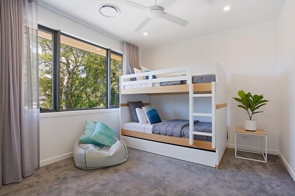 A bunk bed room with a bean bag chair, a small table with a plant, and a window with curtains.