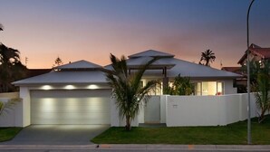 A modern house with a garage, a well-maintained lawn, and a palm tree. - Sanctuary Waterfront – Coastal Elegance in the Heart of Broadbeach Waters (Gold Coast)