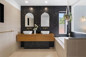A modern bathroom with two sinks, a wooden vanity, a large mirror, and a bathtub. - Effortless Waterfront Living with Heated Pool & Entertainer’s Layout (Gold Coast)