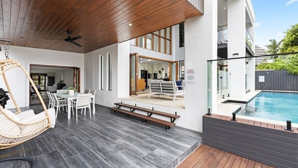 Een modern terras buiten, met een zwembad, houten terras en een eethoek met een hangstoel en tafel.