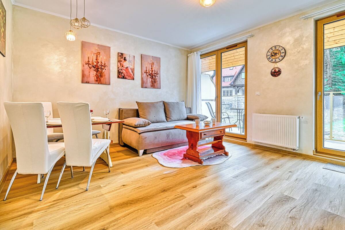 Ein geräumiges Wohnzimmer mit einer Couch, Esstisch und Stühlen, einem Kamin und einem großen Fenster mit Blick ins Freie.