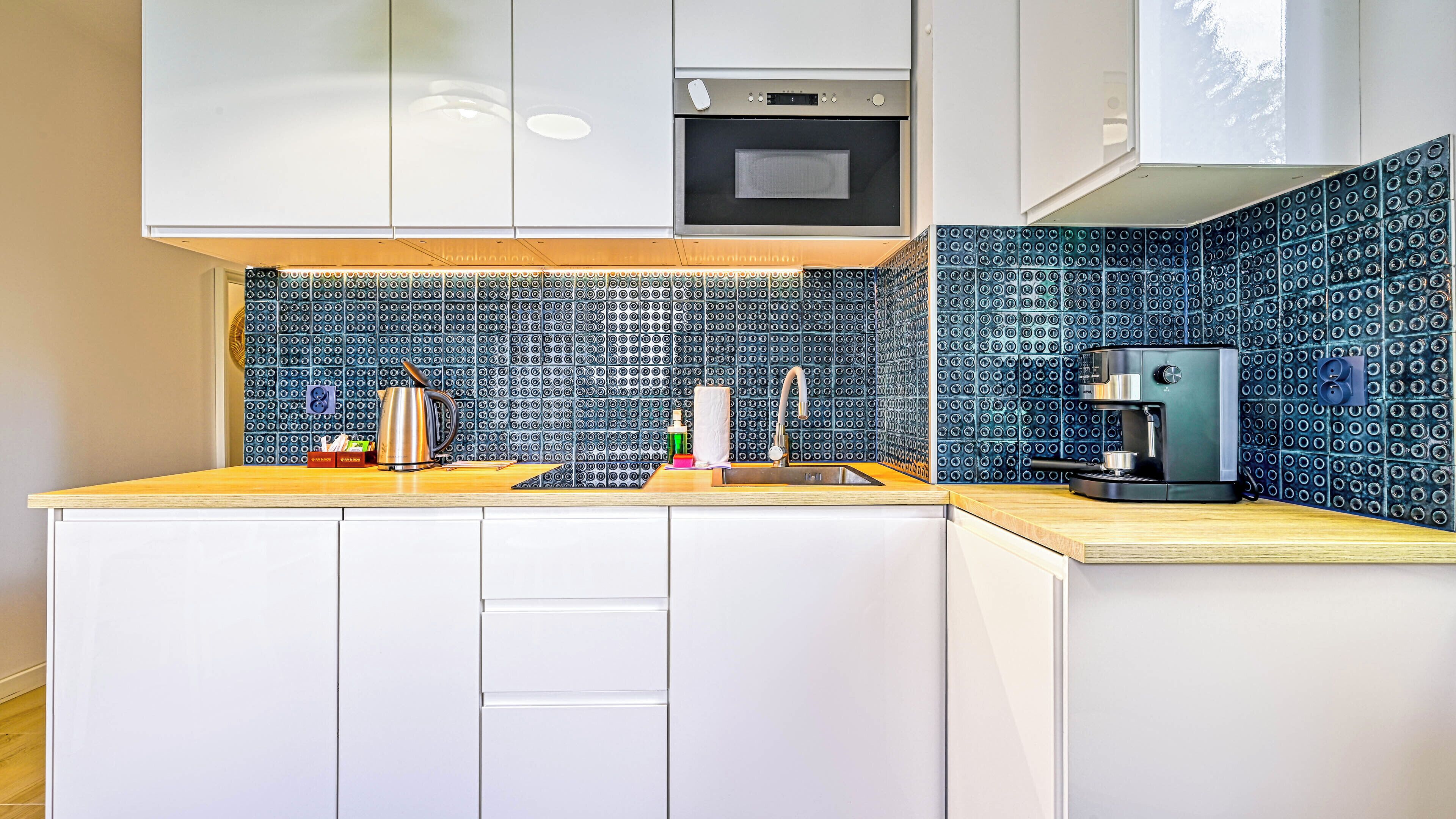 Een moderne keuken met witte kastjes, een roestvrijstalen waterkoker, een koffieapparaat en een decoratieve spatwand.