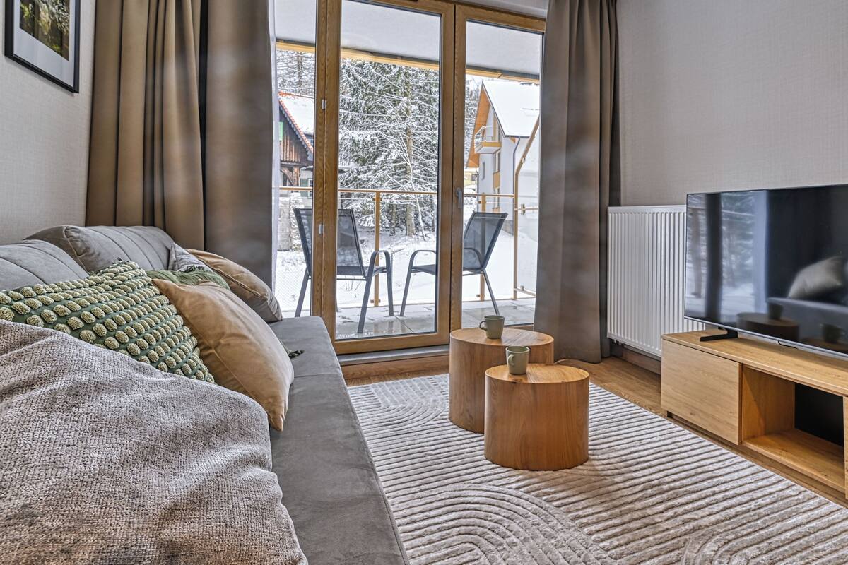 Ein modernes Wohnzimmer mit großem Flachbildfernseher, einer Couch, einem Couchtisch und Blick auf eine verschneite Landschaft.