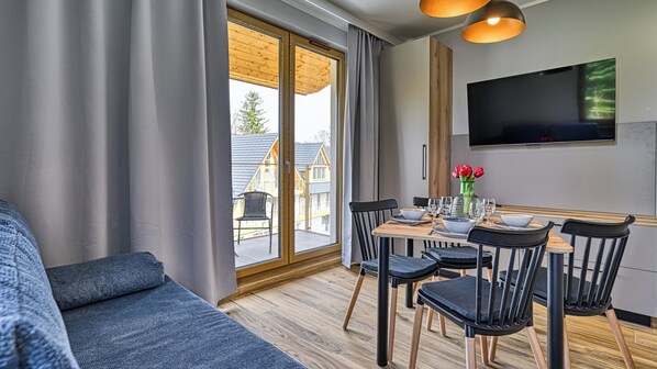 A modern living room with a sofa, dining table set for four, and a TV mounted on the wall.