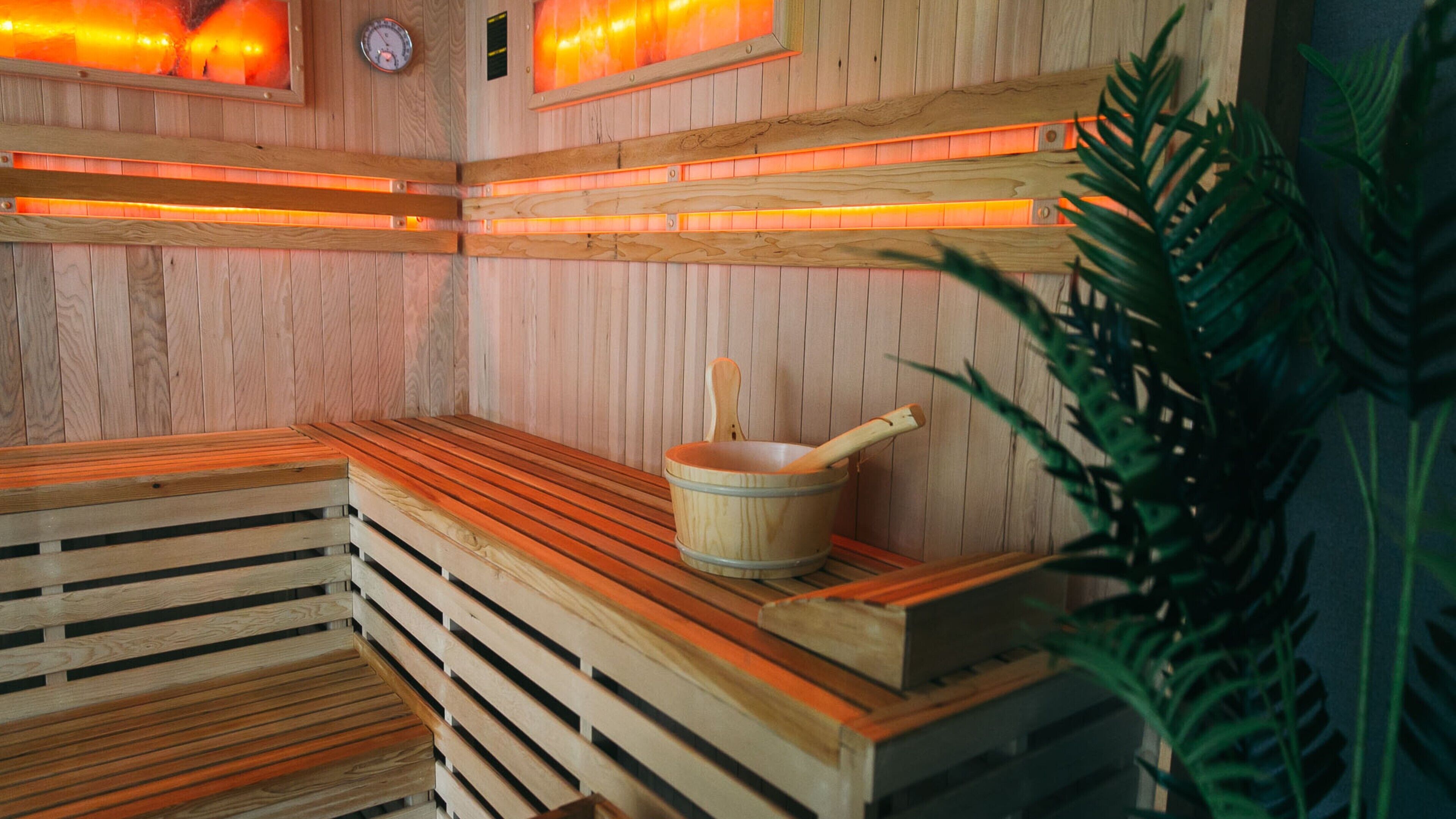 A sauna with wooden benches, a wooden bucket, and a wall-mounted heater.