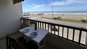 A balcony with a table set for two, overlooking a beach and a road. - Sea view studio in Saint Jean de Monts, parking included (Saint-Jean-de-Monts)
