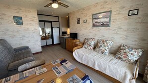 A cozy room with a bed, a sofa, a wooden table with nautical-themed decor, a ceiling fan, and a view of the outside. - Sea view studio in Saint Jean de Monts, parking included (Saint-Jean-de-Monts)