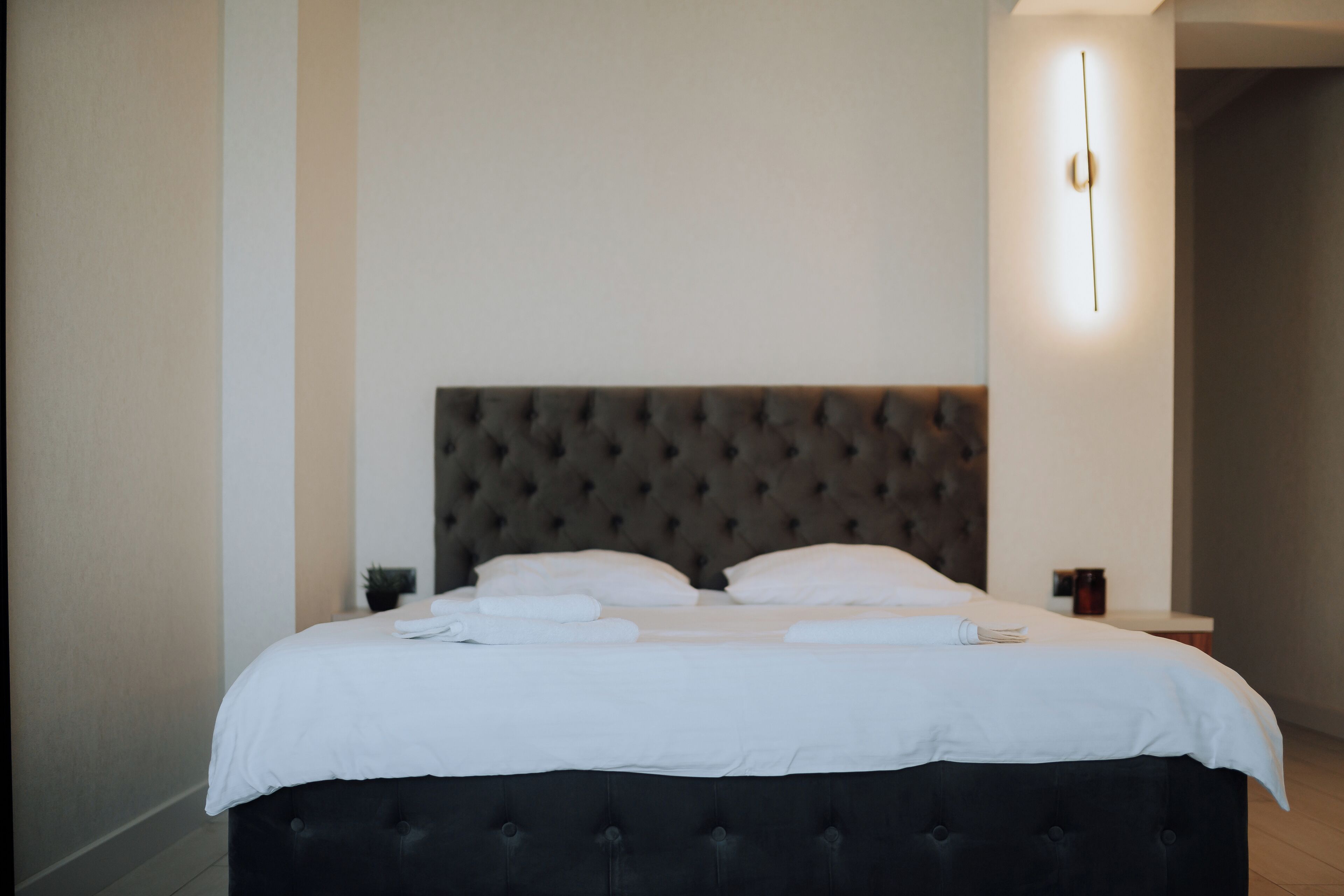 Een net opgemaakt bed met witte lakens en kussens, een gestoffeerd hoofdbord en een nachtkastje met een lamp.