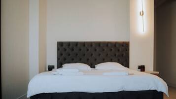 Een net opgemaakt bed met witte lakens en kussens, een gestoffeerd hoofdbord en een nachtkastje met een lamp.
