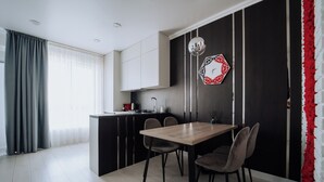 Une cuisine moderne avec un coin repas, comprenant une table et des chaises en bois, un luminaire suspendu et un élément décoratif géométrique sur le mur.