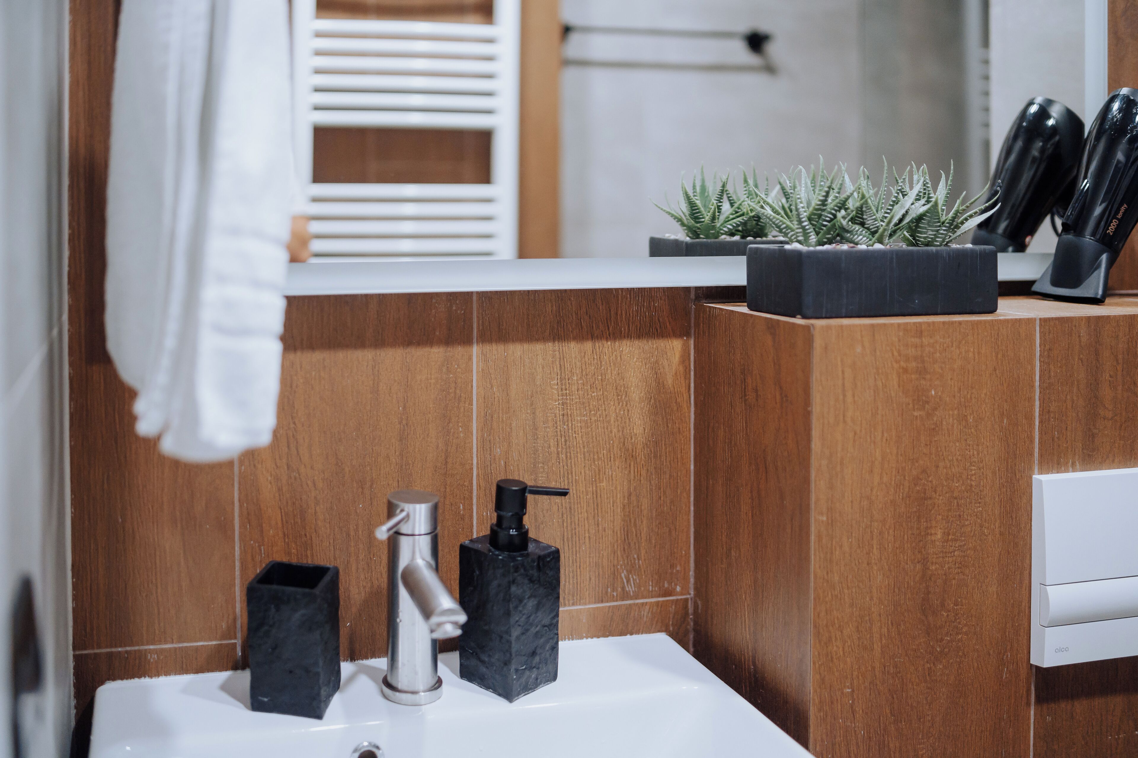 Une salle de bain moderne avec un lavabo blanc, un distributeur de savon en marbre noir et une plante en pot.